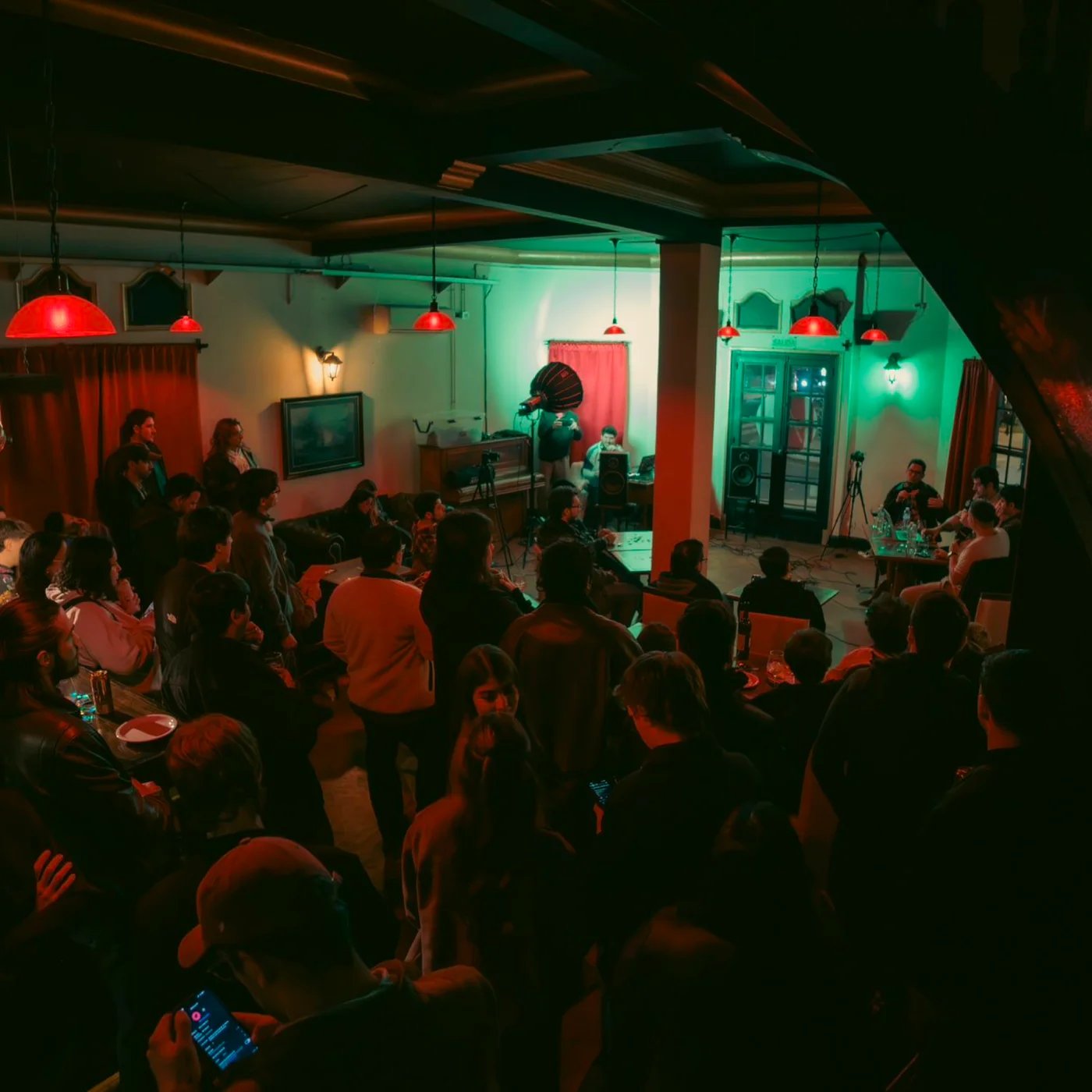 Público reunido alrededor de una charla de SLA en un bar iluminado en verde y rojo